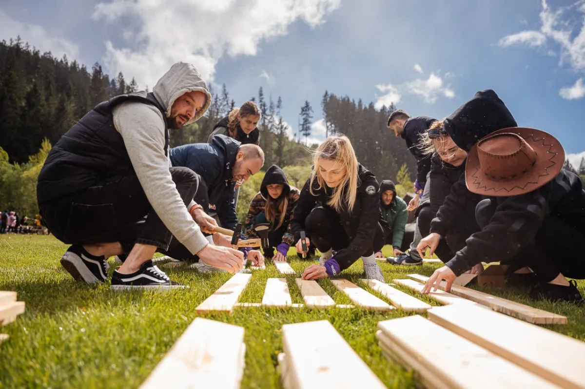 Skupina ľudí pracuje na teambuildingu s drevenými doskami.